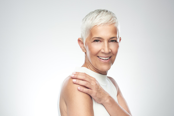 Beautiful smiling senior woman with short gray hair posing in front of gray background. Beauty photography. - Foto, immagini