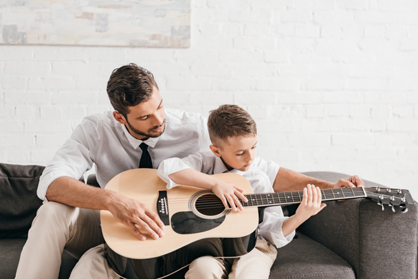 Papa leert zoon om akoestische gitaar thuis te spelen - Foto, afbeelding