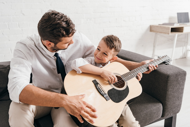 dad teaching son to play acoustic guitar at home - Fotó, kép