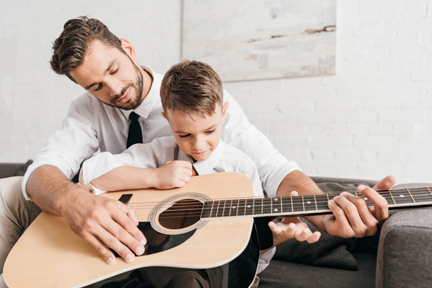 папа учит сына играть на акустической гитаре дома
 - Фото, изображение