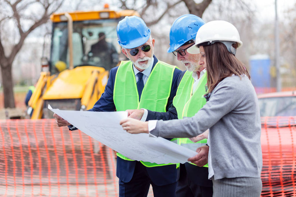 Mixed team of engineers meeting and discussing blueprints while visiting construction site site - Photo, Image