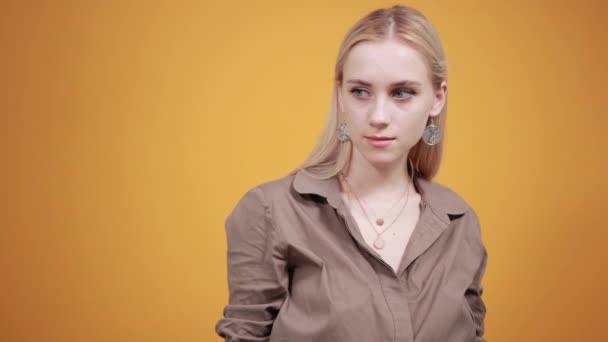 blonde girl in brown blouse over isolated orange background shows emotions - Footage, Video