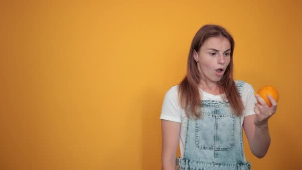 Mladá žena na bílém tričku, nad oranžovým pozadím vykazuje emoce - Záběry, video