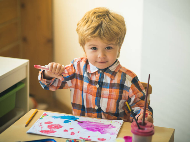 Boy is painting a picture. A beautiful child with felt-tip pens sits at the table and is engaged in creativity and art. Drawing in kindergarten, Childrens development, Art therapy for children. - Foto, afbeelding