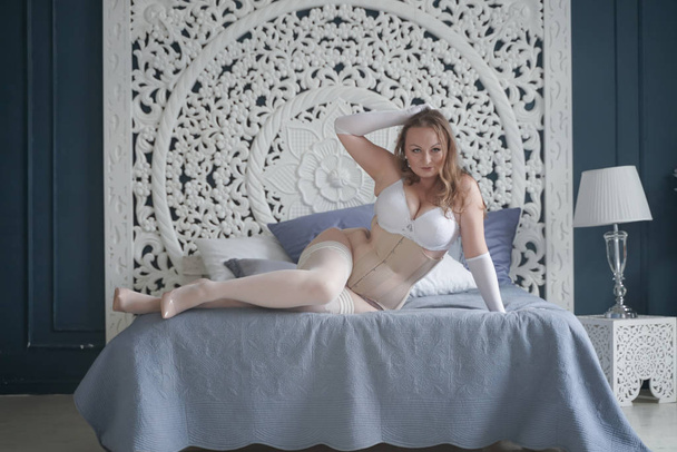 szexuális és méretű menyasszony lány fehér fehérnemű a hálószobában egyedül. pufó nő csipke alsónemű a fűző és a harisnya egyedül - Fotó, kép
