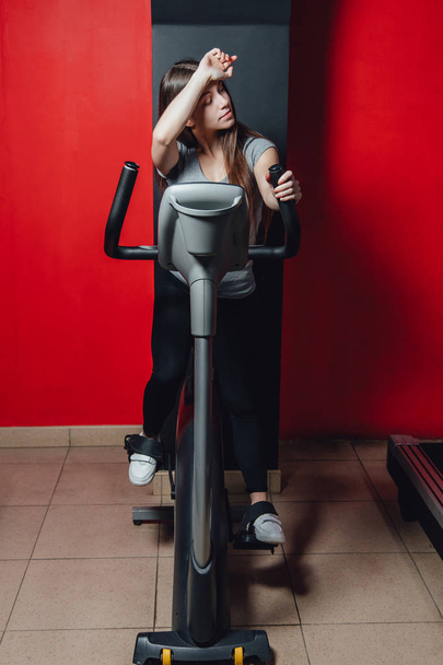 Άσκηση ένα ποδήλατο καρδιοχειρουργική προπόνηση σε μια γυναίκα γυμναστήριο, λαμβάνοντας μια μηχανή απώλειας βάρους με αερόβια για ένα λεπτό και στερεό υγιεινό πρωινό. - Φωτογραφία, εικόνα
