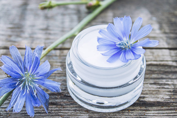 Blue chicory flower and face cream in a glass jar on an old wooden table. Health concept. - Photo, Image