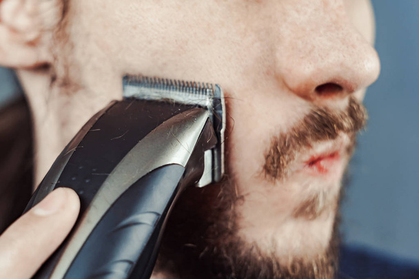 τύπος ξυρίζει το μούσι του με μια ξυριστική μηχανή - Φωτογραφία, εικόνα