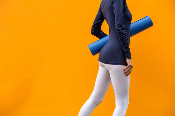 Sporty yoga girl with yoga mat wearing sport clothes over orange background - Photo, image