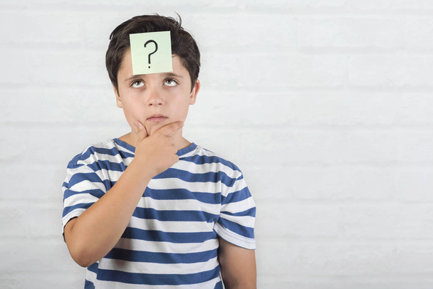 Child thinking with question mark in memo post on his forehead - Foto, Imagem