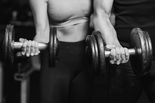Fitness, sports, exercises and weightlifting. Concept - a young woman and a young man with dumbbells sweeping muscles in the gym. - Foto, Bild