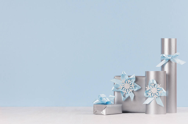 Festive gift boxes for New Year celebration in silver metallic with shiny ribbons and bows on white wood board and pastel blue wall. - Fotoğraf, Görsel