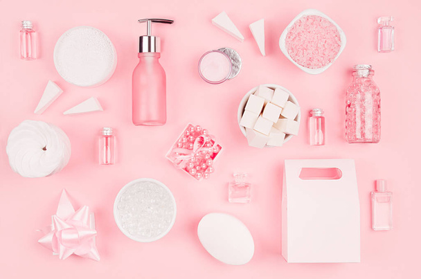 Cosmetic products and accessories in pink color - cream, bath salt, essential oil, soap, towel, sponge, pearls, bottles, bowl on pink background, top view - Photo, image