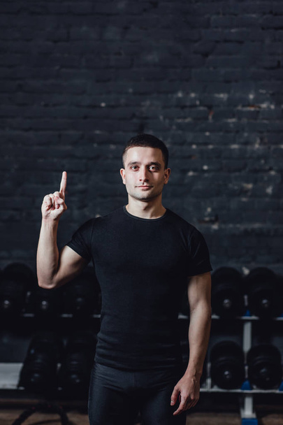 A young athlete is standing in the gym. During this dress, wear a black T-shirt. Standing on a black background and looking away. - Фото, зображення