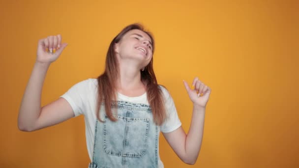 Jovem mulher vestindo camiseta branca, sobre fundo laranja mostra emoções
 - Filmagem, Vídeo