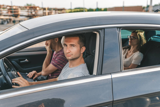 Jeune homme attrayant en t-shirt gris conduisant une voiture avec des amis
 - Photo, image