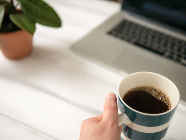 The large mug of coffee in the hand near laptop - Foto, Bild