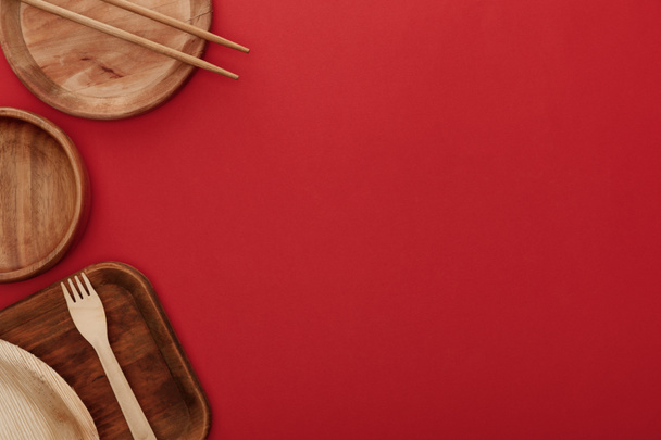 top view of wooden dishes with fork and chopsticks on red background - Φωτογραφία, εικόνα