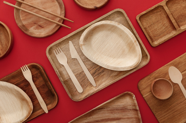 top view of eco-friendly wooden dishes, plates, chopsticks and cutlery on red background - 写真・画像