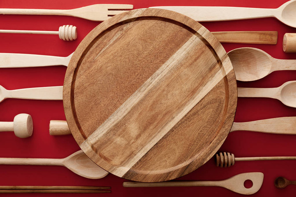 top view of round wooden cutting board on red background with kitchenware - Photo, Image