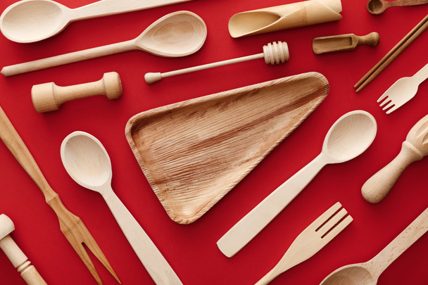 top view of empty triangle wooden dish on red background with kitchenware - Foto, afbeelding