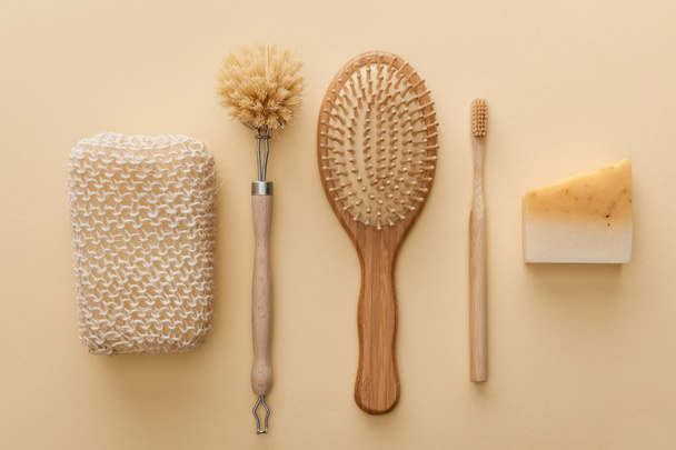 top view of natural bath sponge near toothbrush, hairbrush, body brush and soap on beige background - Photo, image