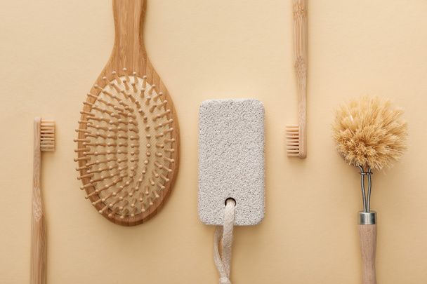 Ansicht von Zahnbürsten, Haarbürste, Körperbürste und Bimsstein auf beigem Hintergrund - Foto, Bild
