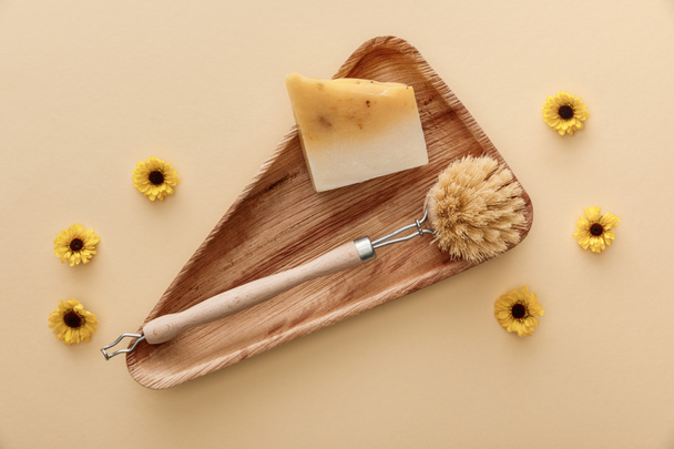 top view of triangle wooden dish with soap and body brush on beige background with flowers - Photo, Image