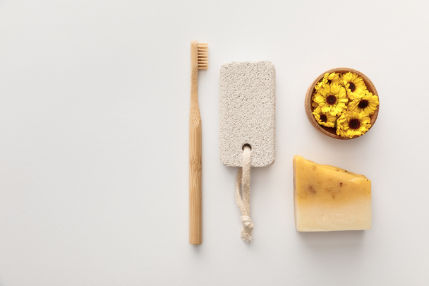 flat lay with toothbrush, piece of soap, pumice stone and cup with flowers on white background - Fotó, kép
