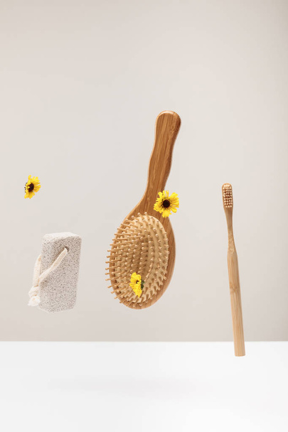 wooden toothbrush, pumice stone, hairbrush and flowers isolated on gray - Photo, Image