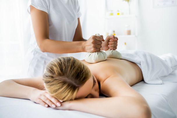 vue recadrée de masseur faisant massage du dos avec des boules à base de plantes à la femme dans le spa
  - Photo, image