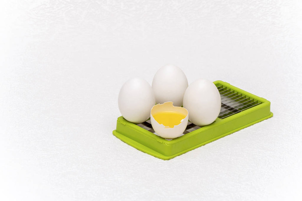 Uova bianche rotte e intere su taglierina da cucina verde su una superficie bianca
 - Foto, immagini