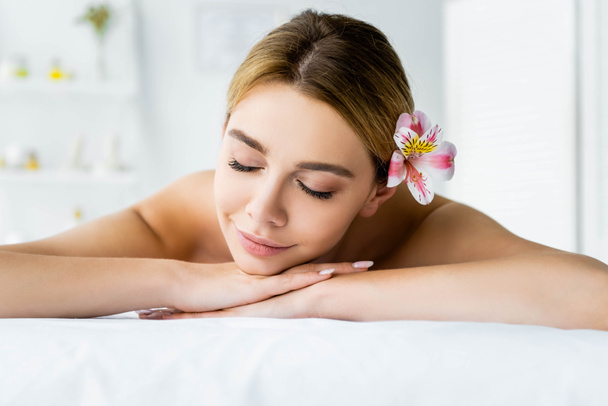attractive woman with flower lying on massage mat in spa  - Photo, Image