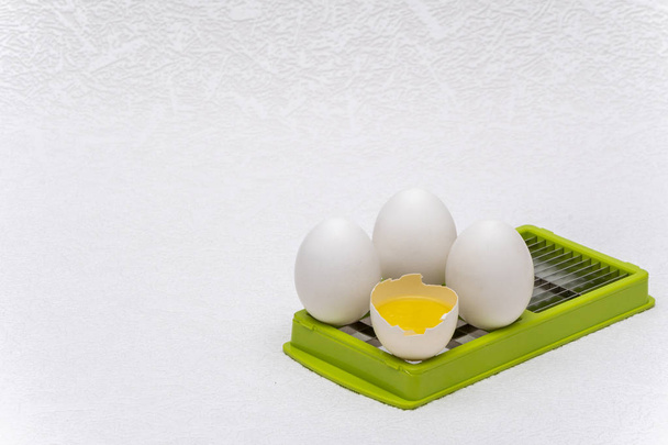 Σπασμένα και ολόκληρα λευκά αυγά σε πράσινο κόφτη κουζίνας σε λευκή επιφάνεια - Φωτογραφία, εικόνα