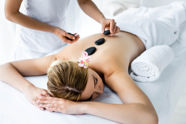 обрізаний вид масажиста робить масаж гарячим каменем для жінки в спа-центрі
  - Фото, зображення