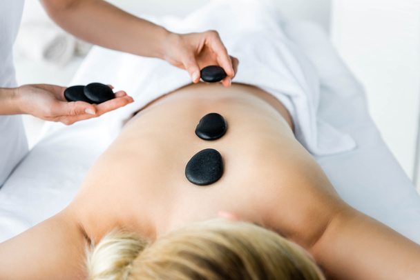 abgeschnittene Ansicht von Masseur tut Hot Stone Massage für Frau im Spa  - Foto, Bild