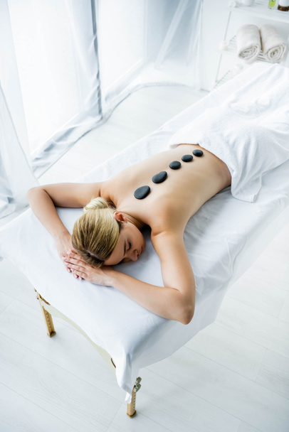 vista ad alto angolo di donna attraente con pietre calde sul retro sdraiato su tappetino da massaggio
 - Foto, immagini