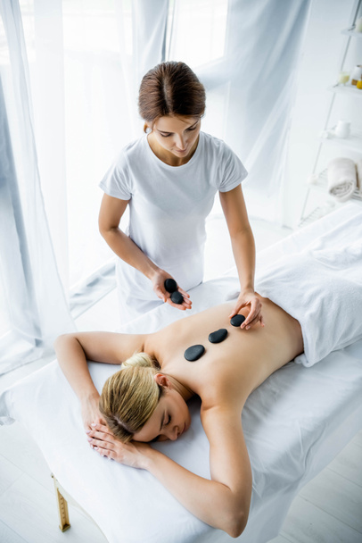 vista de alto ângulo do massagista fazendo massagem de pedra quente para a mulher no spa
  - Foto, Imagem