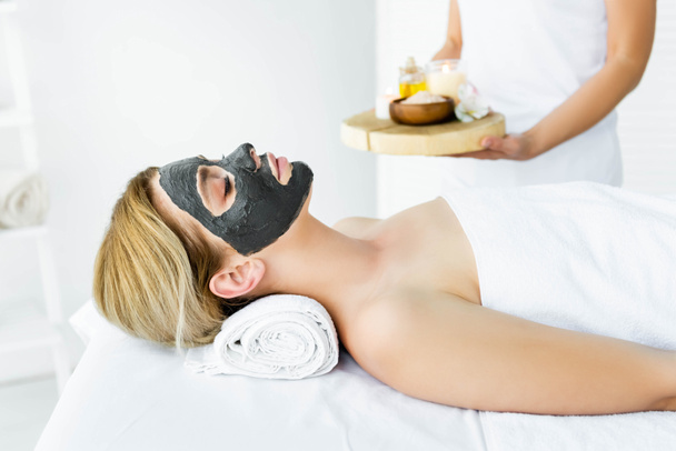ελκυστική γυναίκα με πηλό μάσκα στο πρόσωπο που βρίσκεται στο σπα  - Φωτογραφία, εικόνα