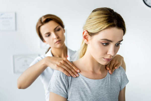 selektivní zaměření chiropraktik dotek ramen přitažlivého pacienta v šedé tričko  - Fotografie, Obrázek
