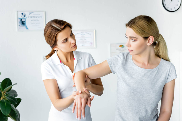 χειροπρακτικός που αγγίζει το χέρι του ελκυστικού ασθενούς με γκρι μπλουζάκι  - Φωτογραφία, εικόνα