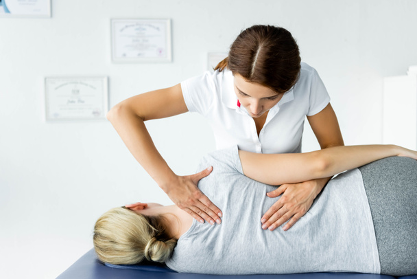 attractive chiropractor touching hand of patient in grey t-shirt  - Foto, immagini