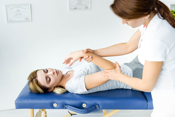 chiropractor touching hand of attractive patient in grey t-shirt  - Foto, Bild
