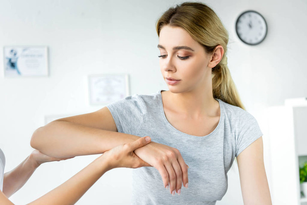 Хиропрактик трогает руку привлекательного пациента в серой футболке
  - Фото, изображение