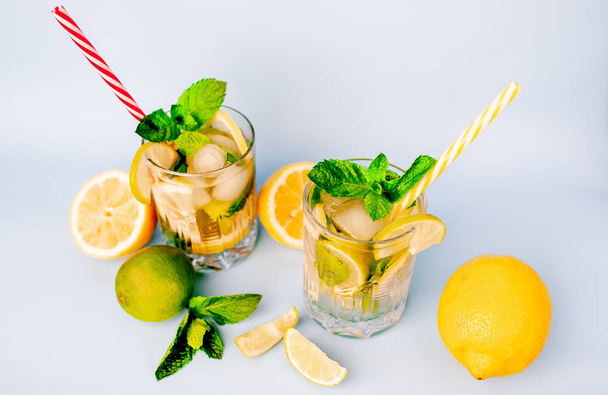 two glasses of lemonade with lime, lemon and mint leaves, ice cubes and straws on white - 写真・画像