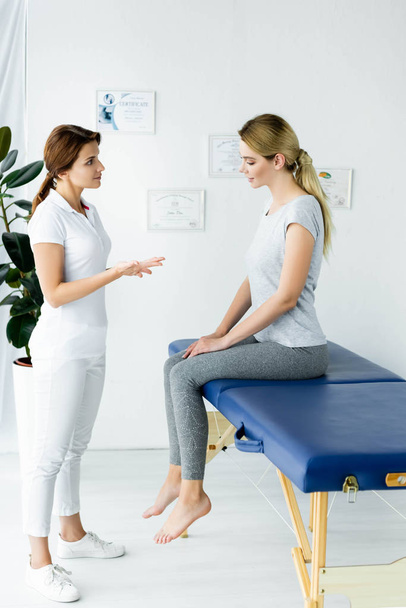chiropractor talking with attractive patient in t-shirt in clinic  - Foto, Bild