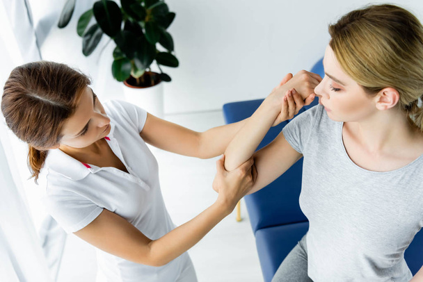 high angle view of chiropractor touching hand of patient in grey t-shirt in clinic  - Fotografie, Obrázek