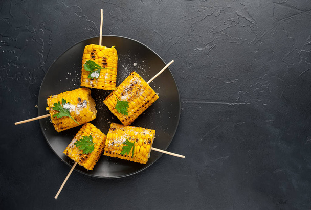 grilled pieces of corn with salt in plate on black table - Photo, Image