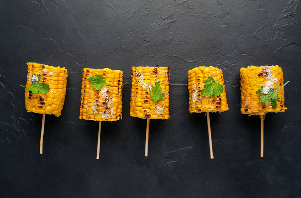 grilled pieces of corn with salt on black table - 写真・画像