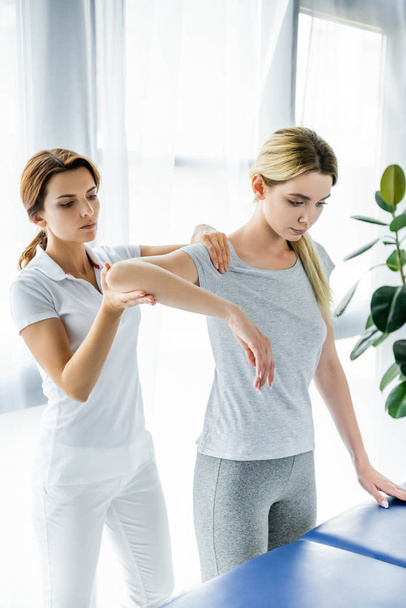 chiropractor touching shoulders of attractive patient in grey t-shirt  - Fotografie, Obrázek